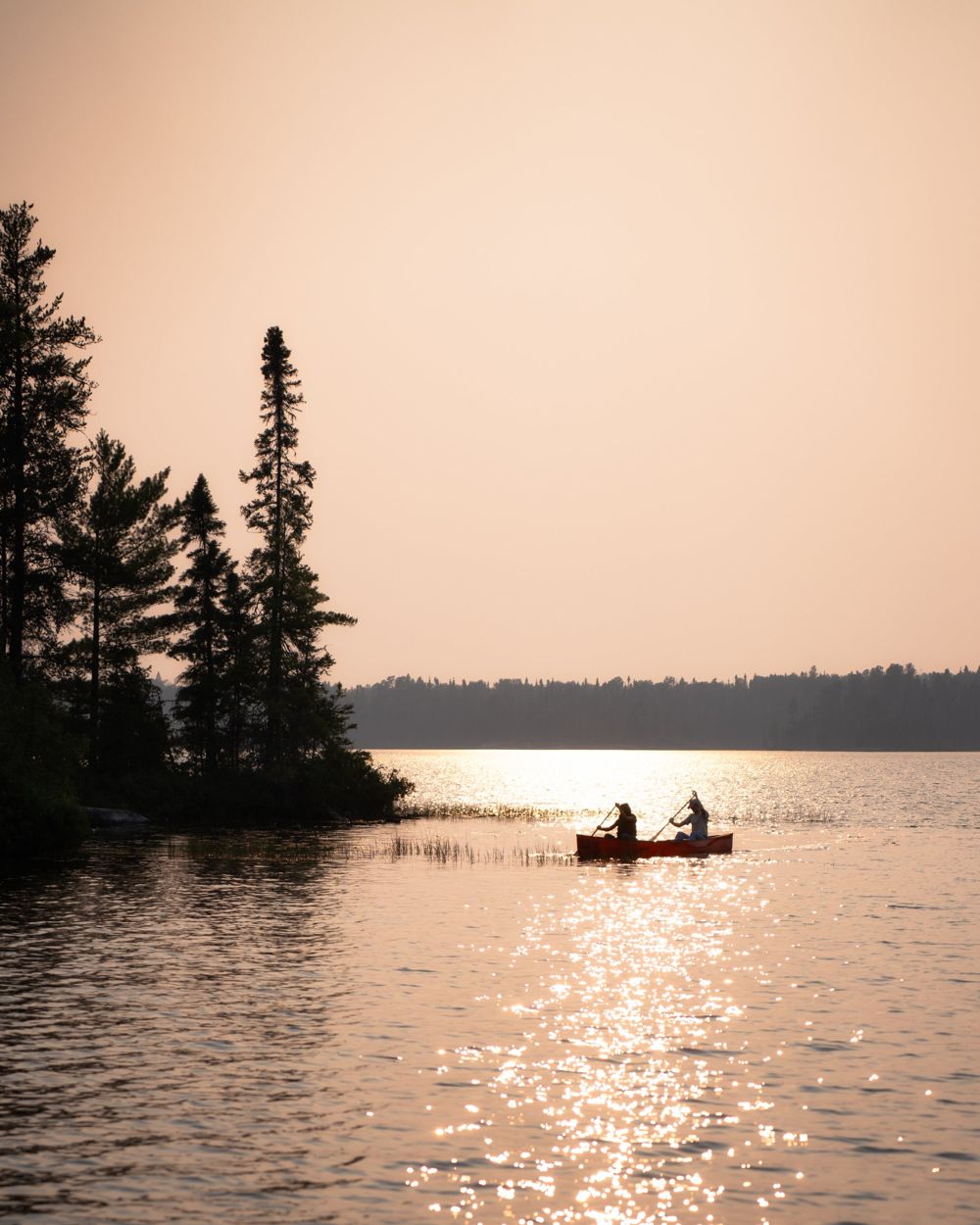 Two people paddling a canoe on a lake at sunset