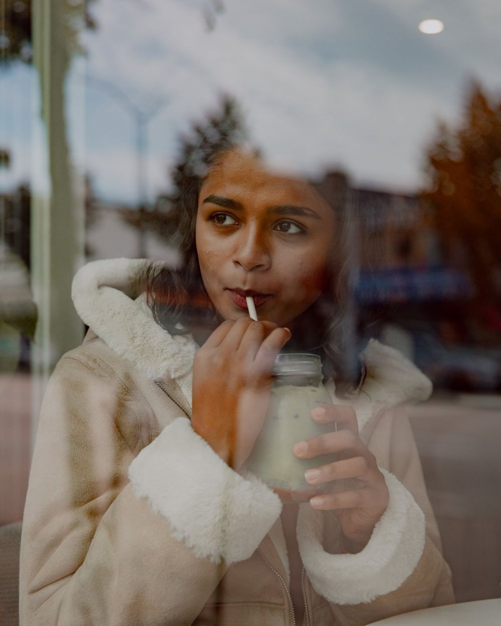 Sriya sipping an iced matcha by a café window