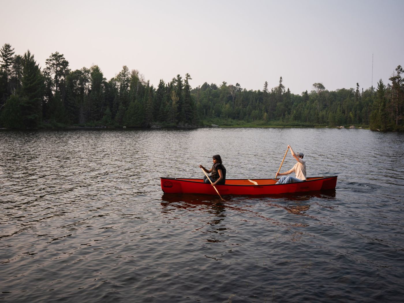 Two people paddling a red canoe on a northern lake