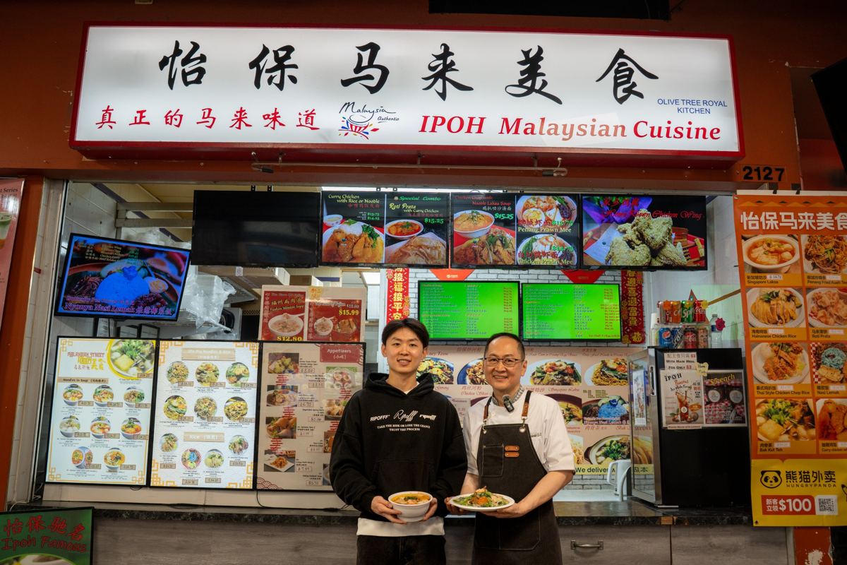 Chef and owner of IPOH Malaysian Cuisine holding dishes in front of their food court stall