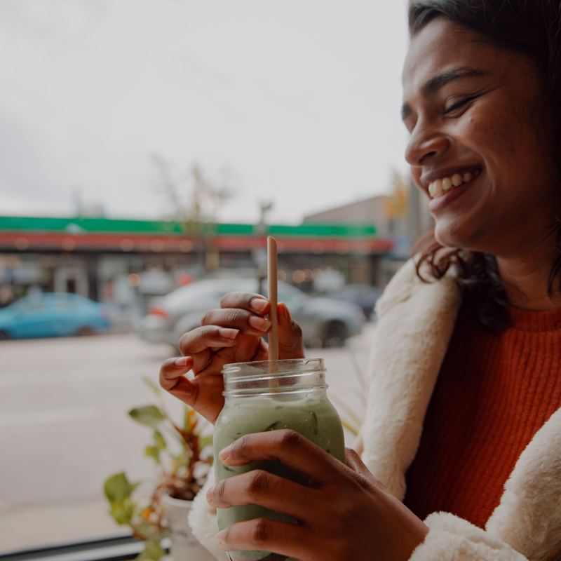 Sriya laughing with an iced matcha at a café window